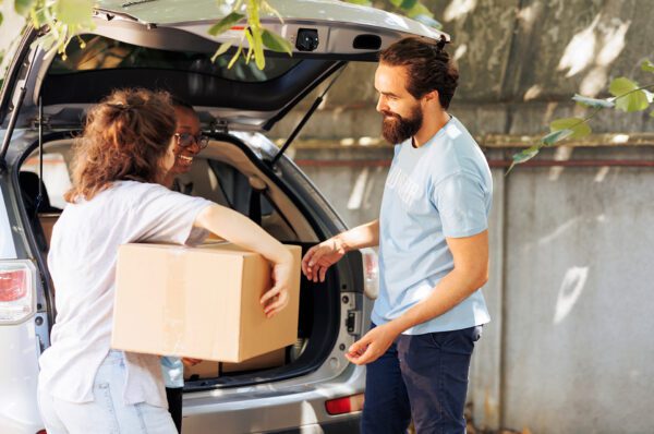 Two people loading a cardboard box into the back of a car as part of The Laptop Initiative, supporting technology reuse and digital inclusion.